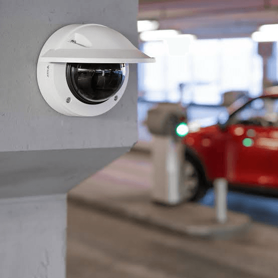 White dome security camera with sunshield mounted on a concrete pillar in a parking garage.