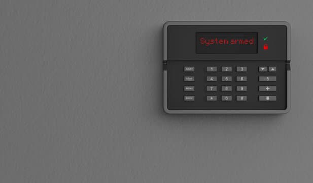 Black home security keypad on a gray wall with red text displaying "System armed."