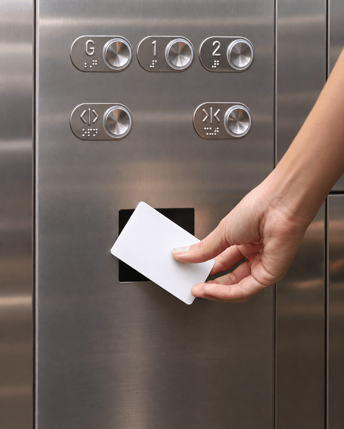 Hand holding a white key card against a reader on a stainless steel elevator panel.