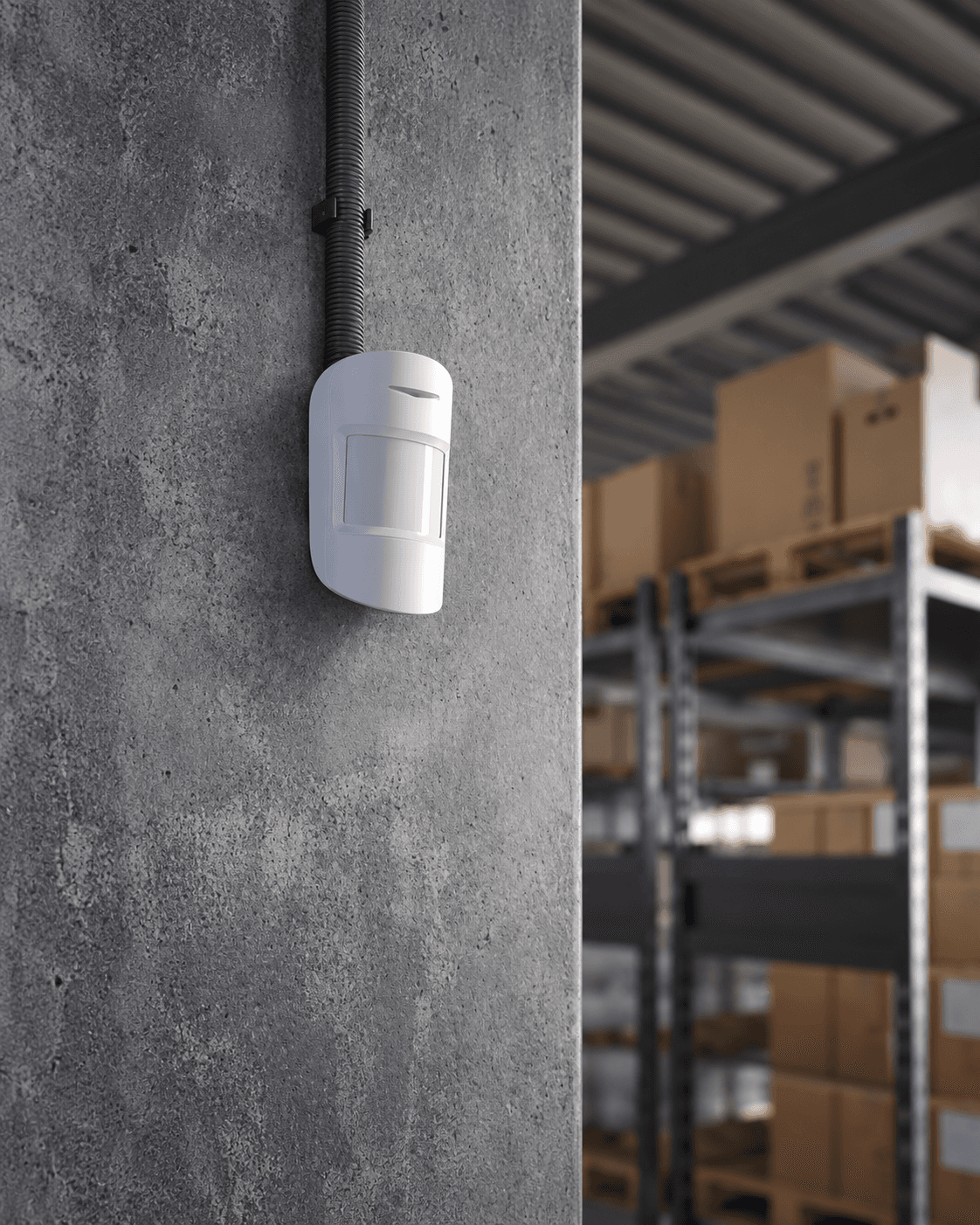 White motion sensor mounted on a concrete wall in a warehouse with storage boxes.