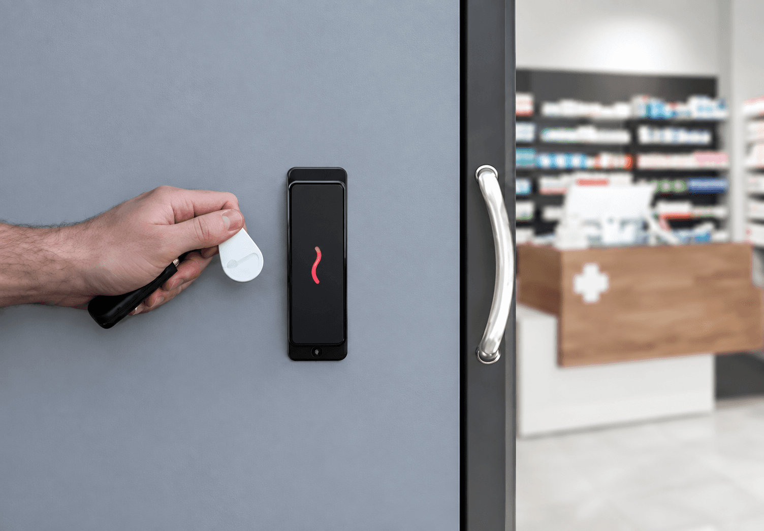 Hand holding a white key fob near a black electronic reader at a pharmacy.