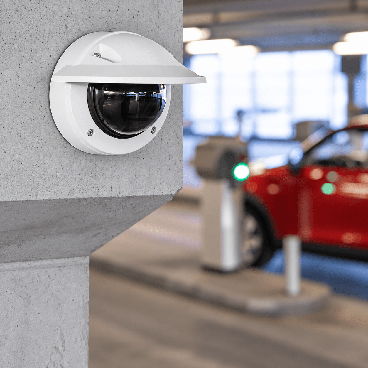 White dome security camera mounted on a concrete pillar overlooking a blurred parking garage.