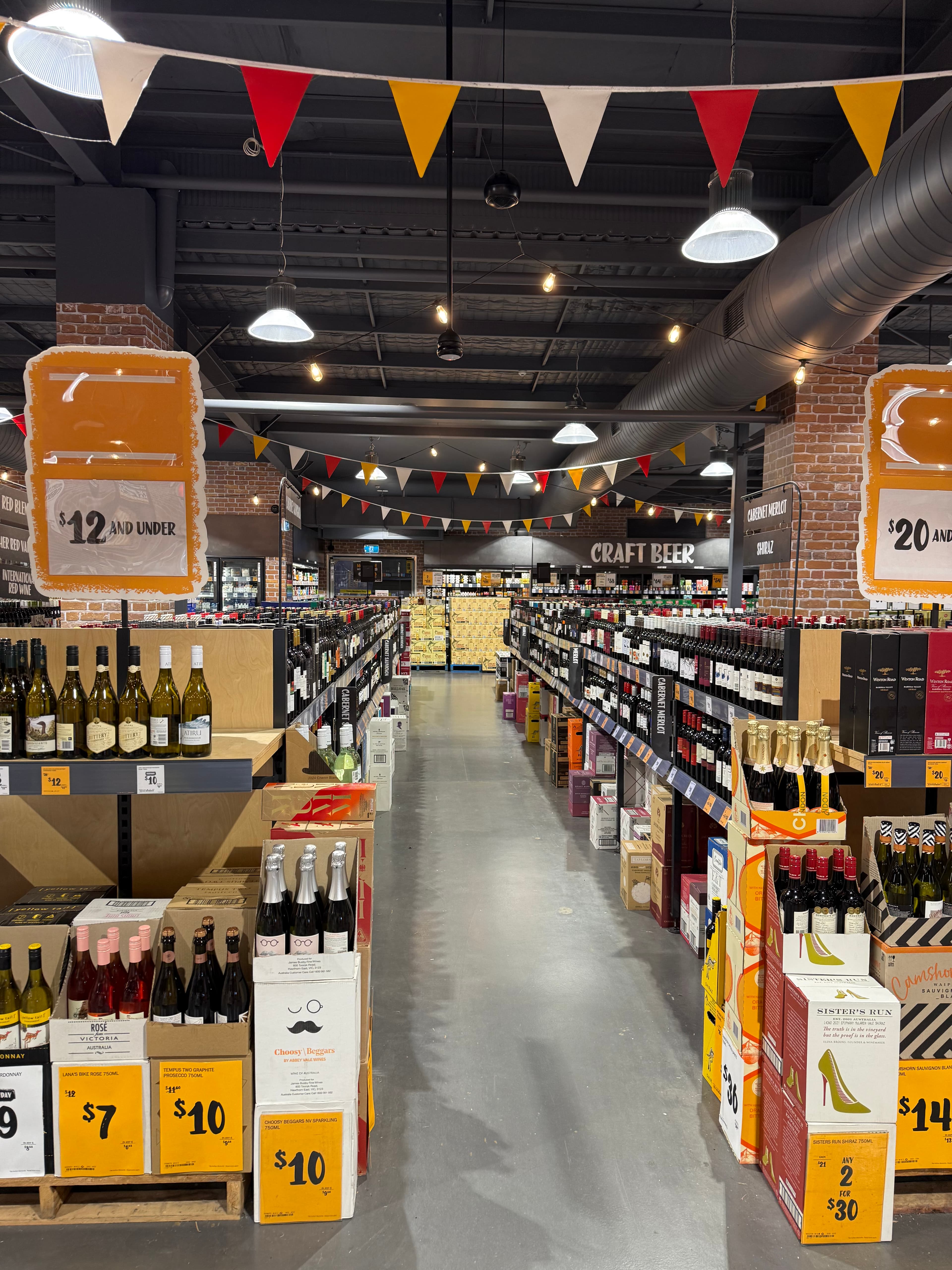 Liquor store aisle with shelves of wine, craft beer, and festive bunting hanging overhead.
