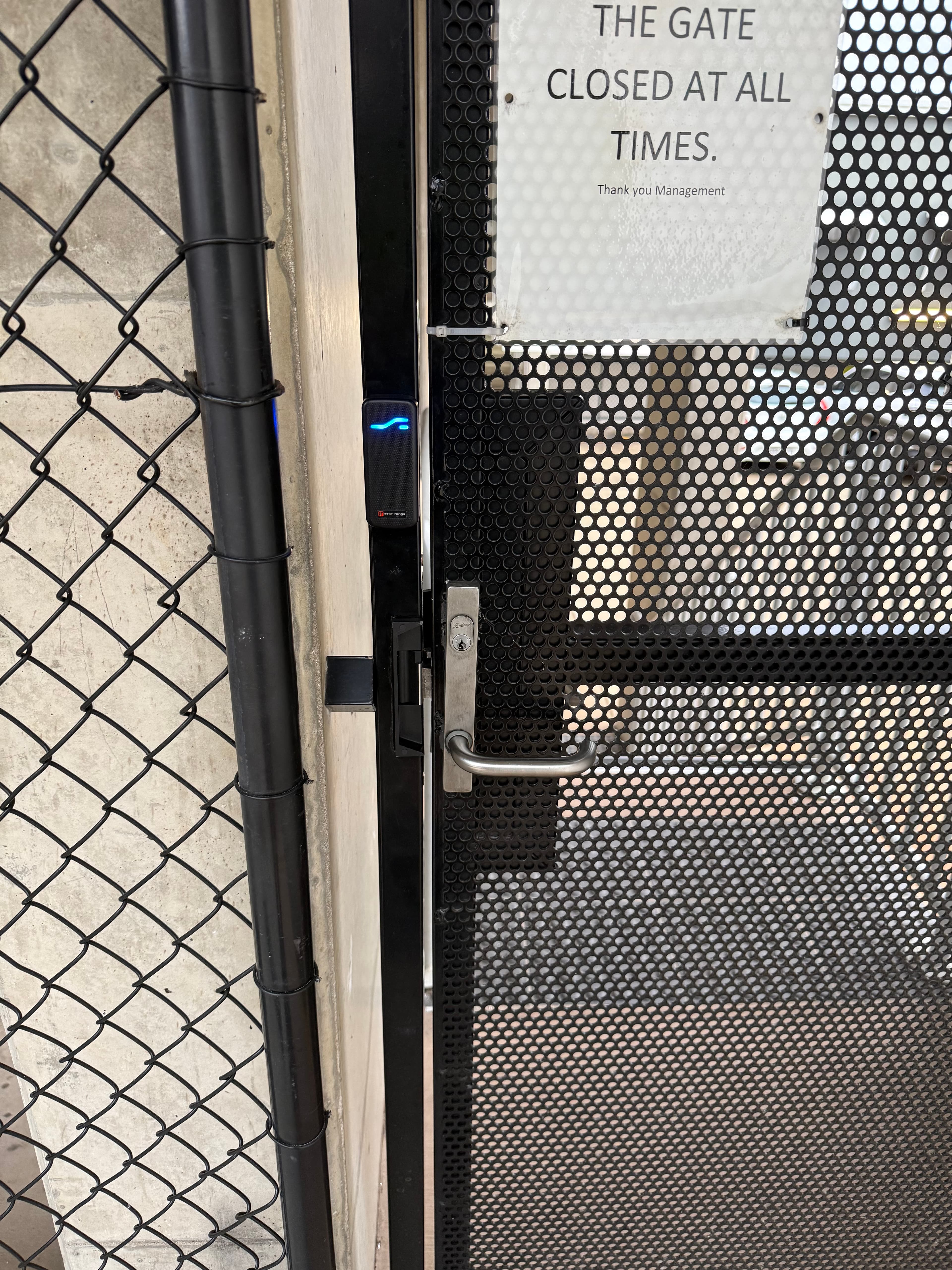 Perforated metal gate with a silver handle, blue-lit card reader, and a closure sign.