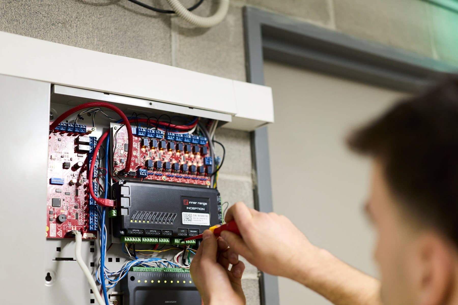 Technician using a screwdriver to connect wires inside an open security system control panel.