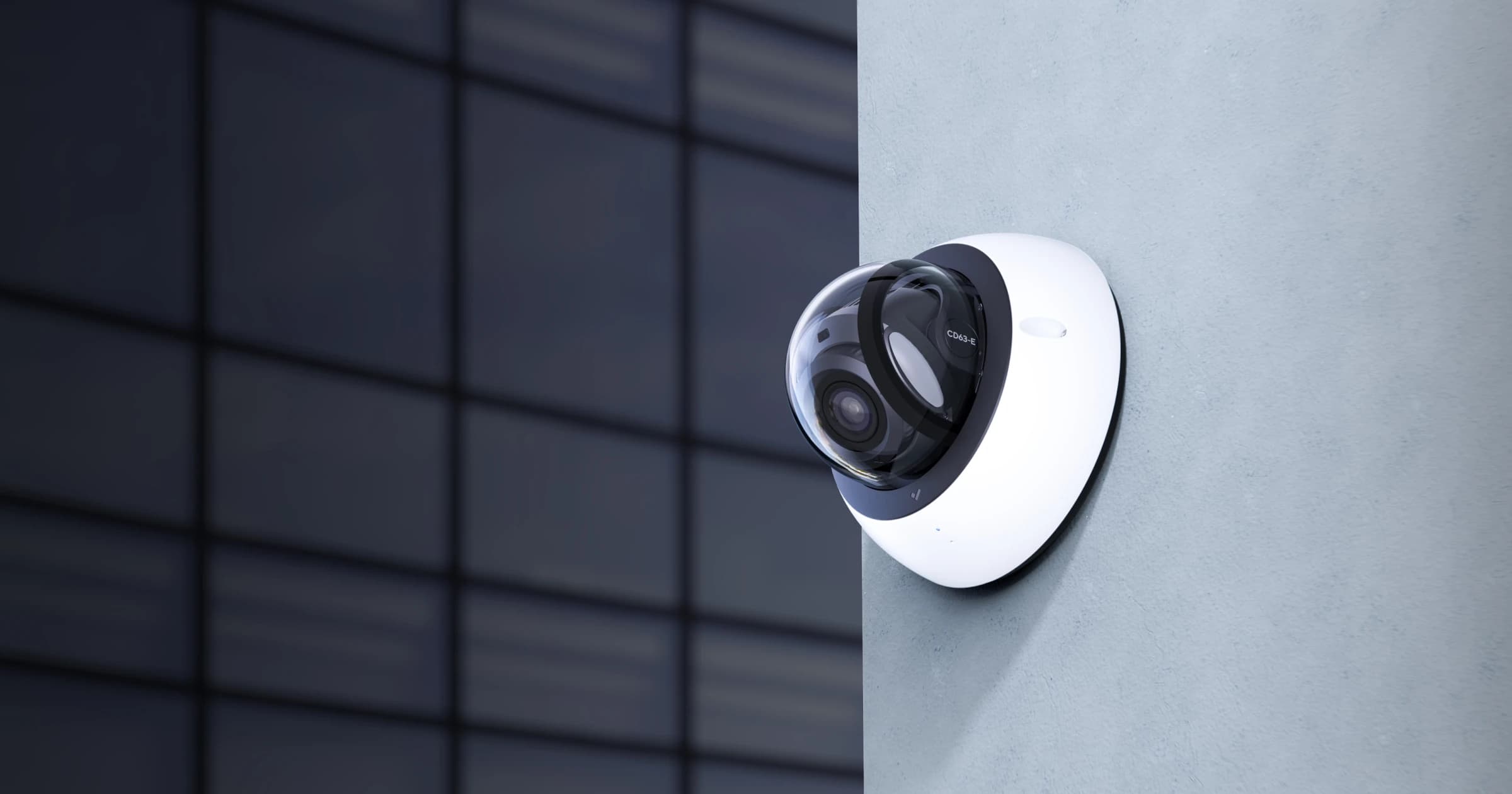 White dome security camera mounted on a gray wall with a blurred office building background.