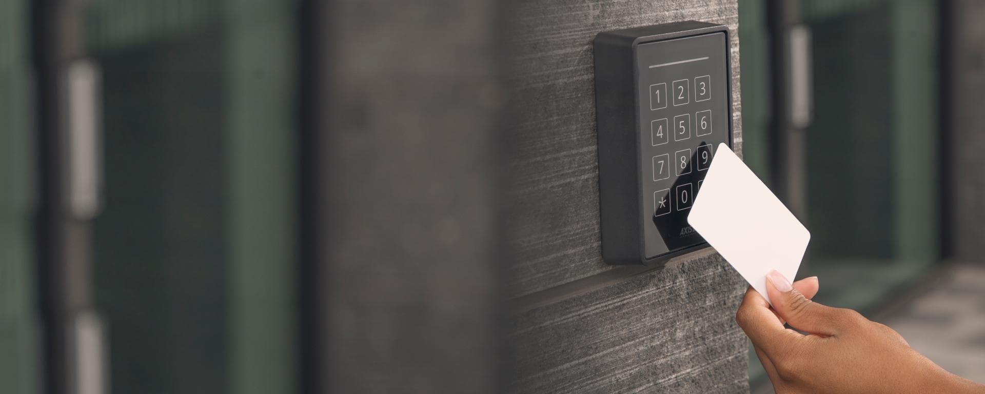 Hand holding a white access card near a black electronic keypad on a stone wall.