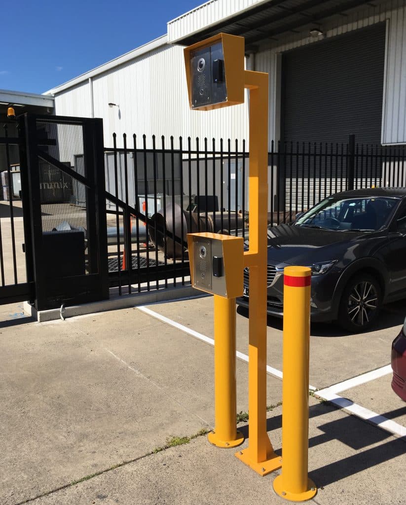 Dual-height yellow intercom system for trucks and cars at a gated industrial facility entrance.