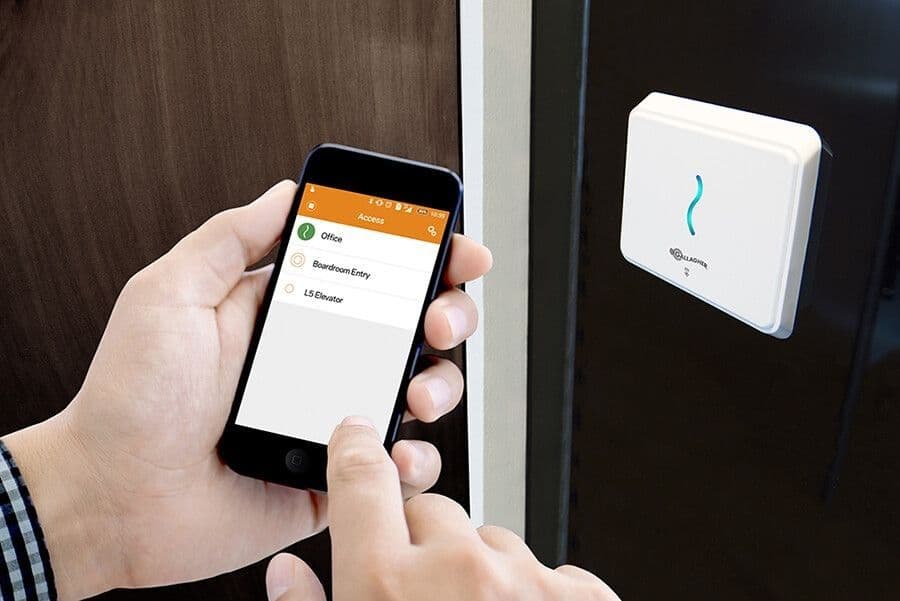 A person uses a smartphone app to gain entry through a wall-mounted security reader.