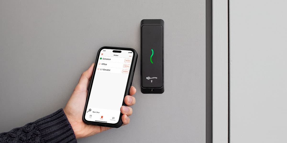 Hand holding a smartphone with an access app near a Gallagher wall-mounted security reader.