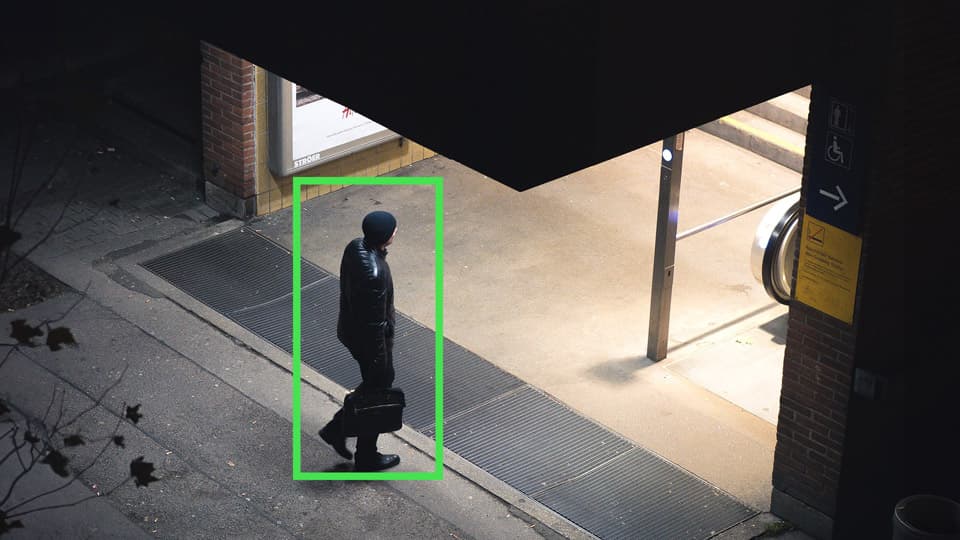 Man in black clothing carrying a briefcase walks past a lit subway entrance at night.