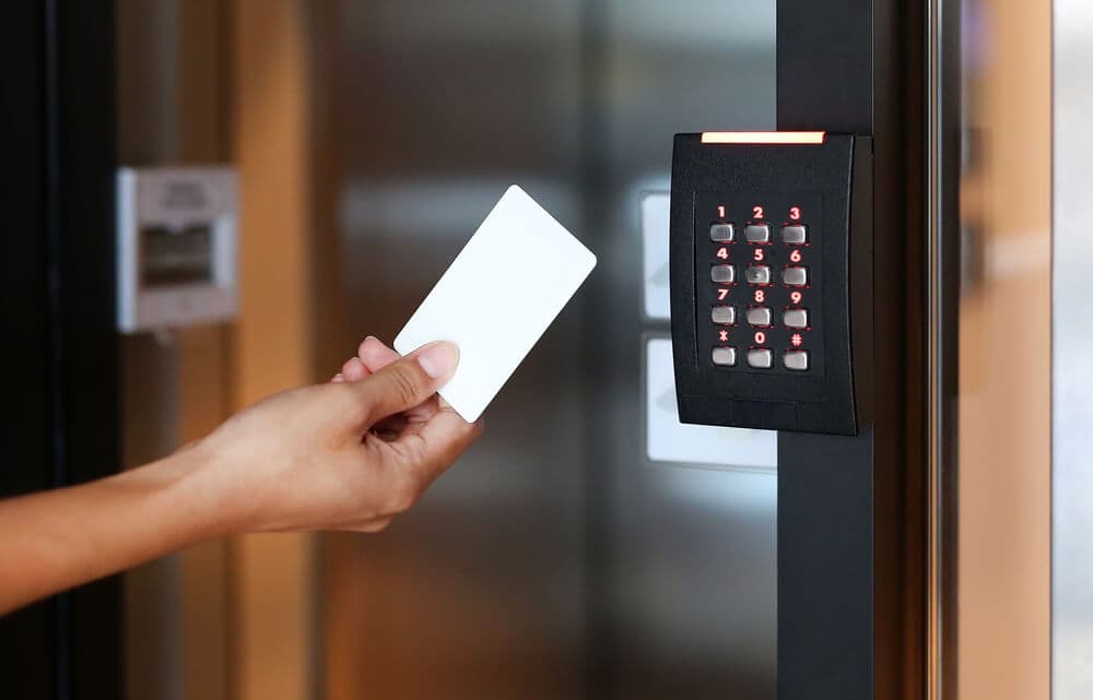 Hand holding a white key card near a black electronic keypad with glowing red numbers.