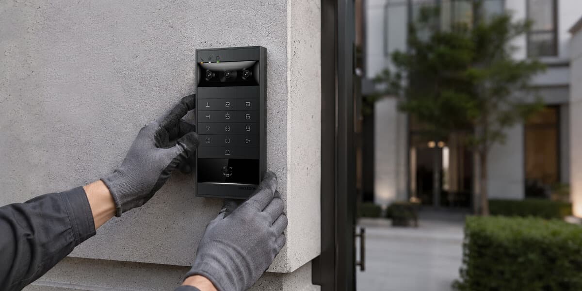 Gloved hands installing a black Hikvision intercom with a keypad on a concrete wall.
